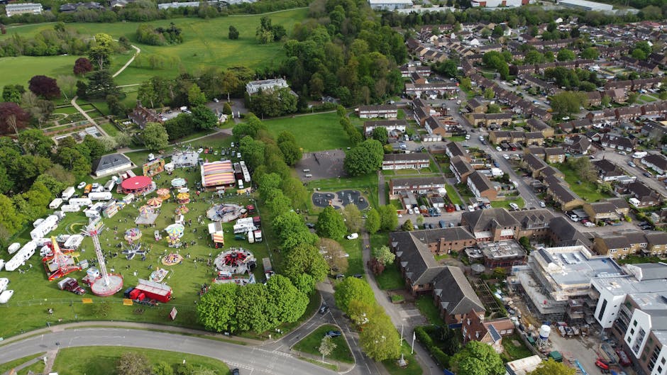 The image shows a wide, open grassy area within Nonsuch Park, bordered on both sides by dense, lush green deciduous trees with full canopies. The grass appears freshly mowed and is a mix of green and